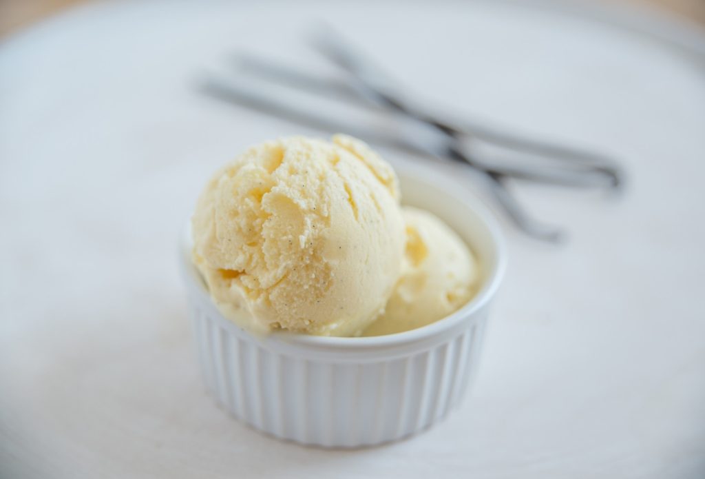 A bowl of Vanilla Bean Ice Cream with Vanilla beans sitting in the background 