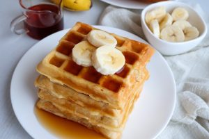 A stack of gluten-free waffles topped with syrup and bananas
